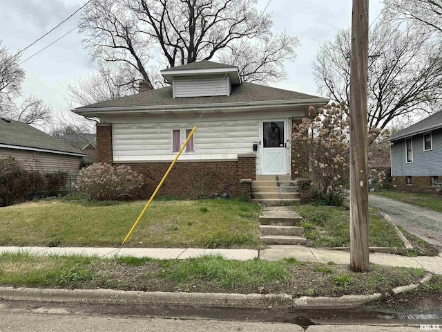 bungalow-style house featuring roof with shingles, brick siding, entry steps, and a front lawn