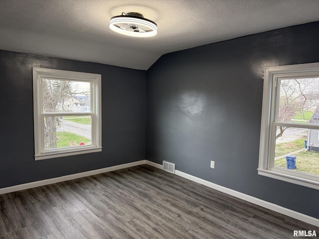 spare room featuring visible vents, a textured ceiling, plenty of natural light, and dark wood finished floors