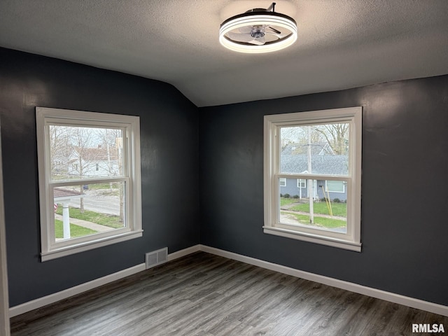 empty room featuring visible vents, a wealth of natural light, and wood finished floors