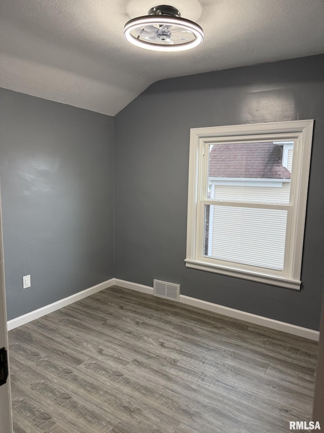 empty room with a textured ceiling, wood finished floors, baseboards, and visible vents
