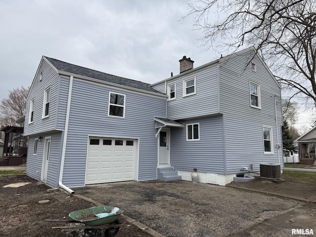 rear view of house featuring a chimney, an attached garage, aphalt driveway, central AC unit, and entry steps