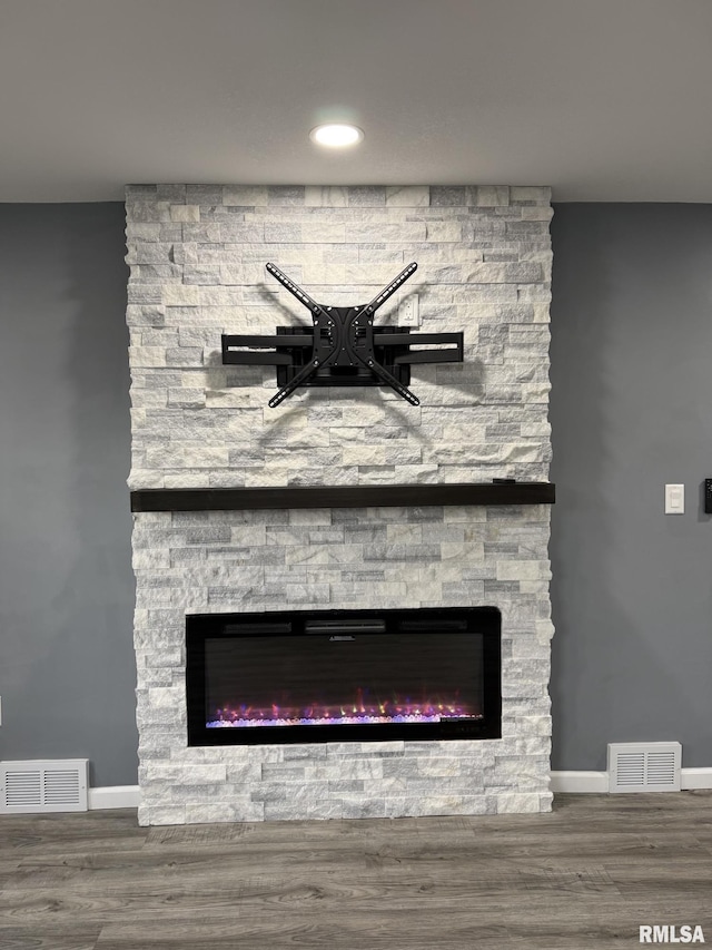 interior details featuring visible vents, a stone fireplace, baseboards, and wood finished floors