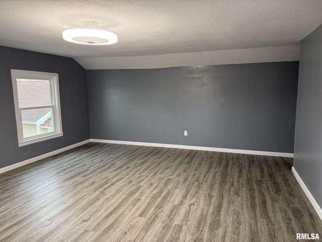 empty room featuring baseboards, a textured ceiling, wood finished floors, and lofted ceiling