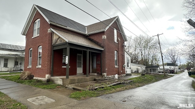 view of front of house featuring roof with shingles, brick siding, and covered porch