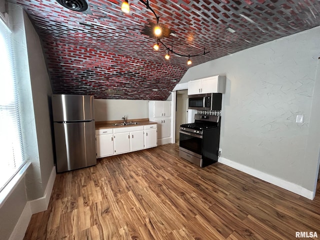 kitchen featuring white cabinetry, baseboards, appliances with stainless steel finishes, and vaulted ceiling
