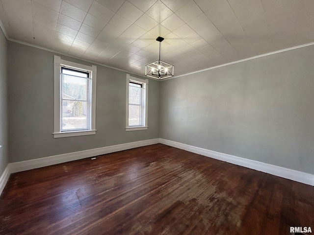 spare room with dark wood-type flooring, crown molding, a notable chandelier, and baseboards