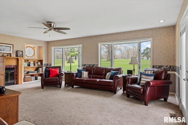 living area with light carpet, a tiled fireplace, and ceiling fan