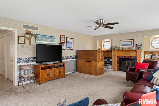 living room with wallpapered walls, light carpet, a ceiling fan, visible vents, and a brick fireplace