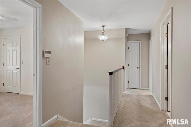 hallway with baseboards, an upstairs landing, and light colored carpet