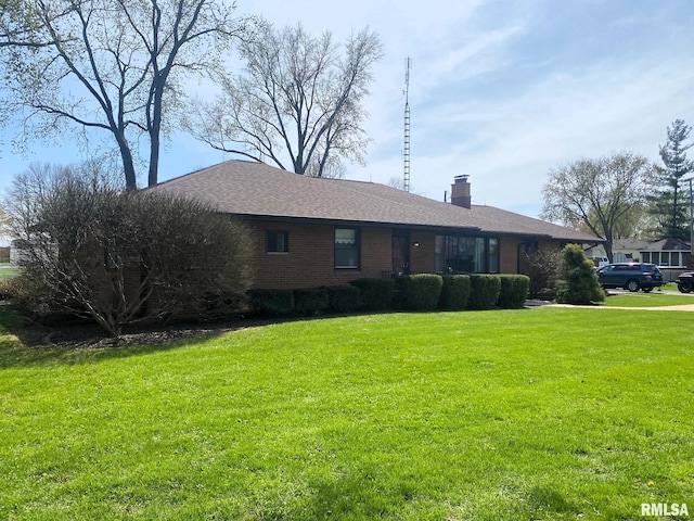 ranch-style home with a chimney, a shingled roof, and a front lawn
