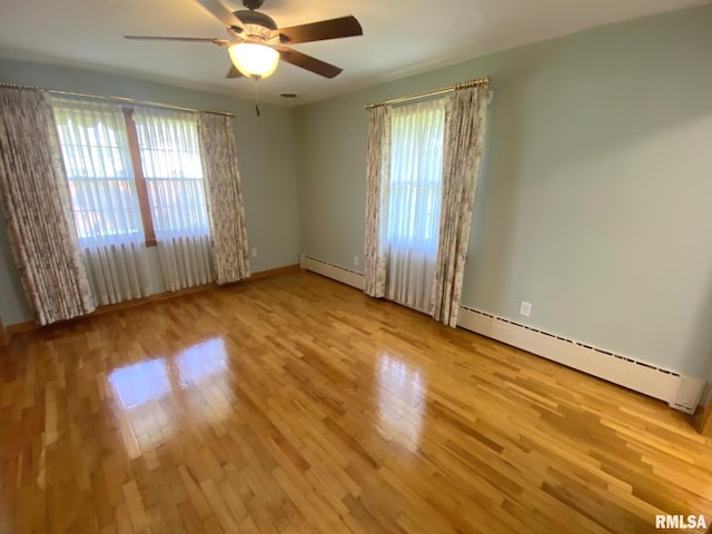 unfurnished room with a wealth of natural light, wood finished floors, and baseboard heating