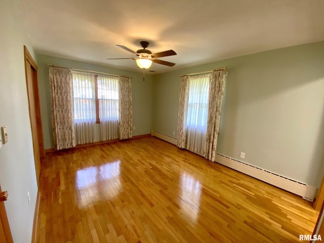 spare room featuring a wealth of natural light, a baseboard heating unit, a ceiling fan, and wood finished floors