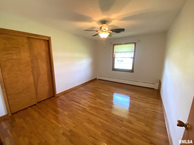 unfurnished bedroom featuring a closet, baseboards, a ceiling fan, wood finished floors, and a baseboard heating unit