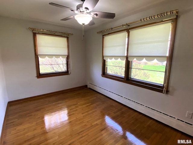 spare room featuring baseboard heating, wood finished floors, ceiling fan, and plenty of natural light