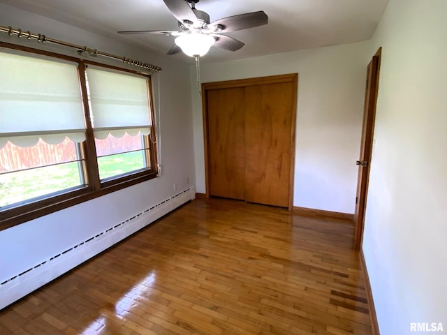 unfurnished bedroom featuring a closet, a baseboard heating unit, baseboards, a ceiling fan, and light wood-style floors