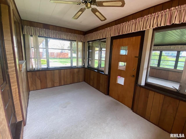 unfurnished sunroom featuring wood walls, carpet, and a ceiling fan