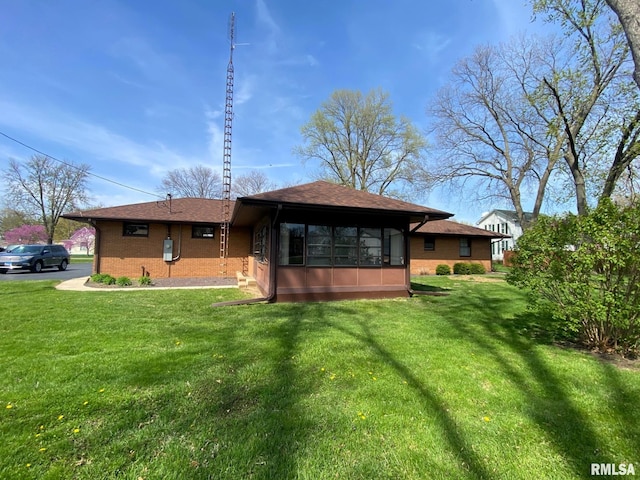 rear view of property with a sunroom, roof with shingles, brick siding, and a lawn