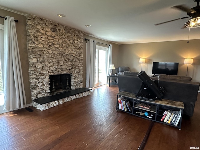 living area featuring a stone fireplace, ornamental molding, a ceiling fan, visible vents, and wood finished floors