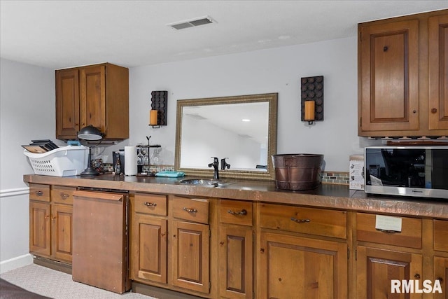 kitchen with visible vents, stainless steel microwave, a sink, dark countertops, and brown cabinets
