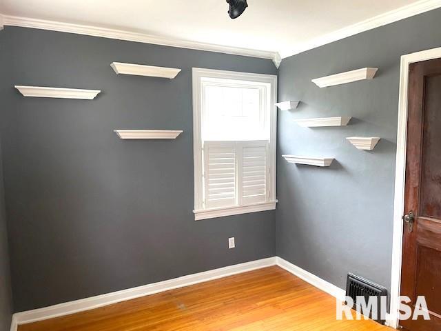 interior space with wood finished floors, baseboards, ornamental molding, and visible vents