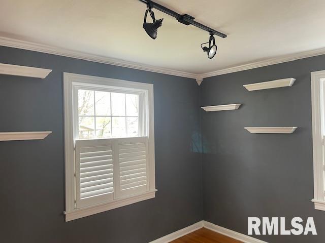 empty room featuring ornamental molding, baseboards, and rail lighting