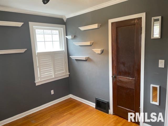 spare room with crown molding, wood finished floors, baseboards, and visible vents