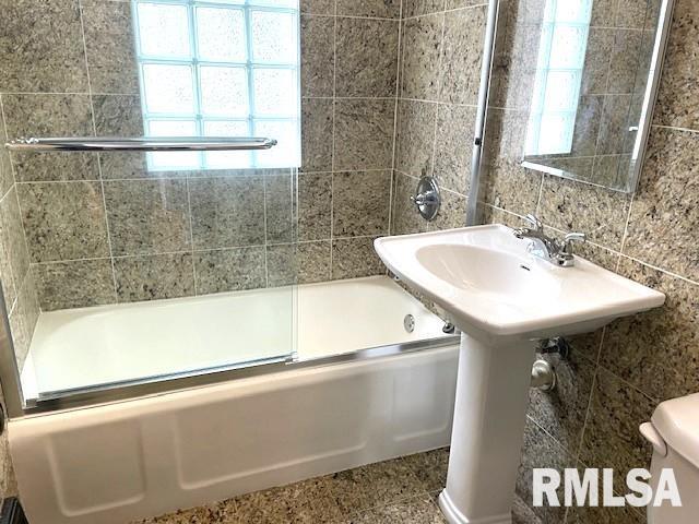 full bath featuring toilet, tile patterned floors, shower / bath combination with glass door, and tile walls