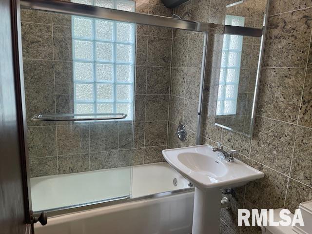 bathroom with toilet, shower / bath combination with glass door, and tile walls