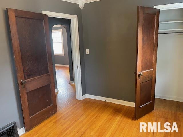 unfurnished bedroom with arched walkways, visible vents, baseboards, and light wood-style flooring