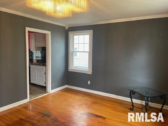 empty room with crown molding, baseboards, an inviting chandelier, and wood finished floors