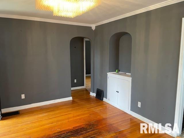 empty room with arched walkways, baseboards, ornamental molding, and wood finished floors