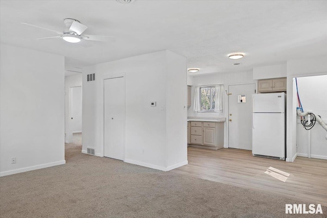 unfurnished living room with light carpet, visible vents, baseboards, and ceiling fan