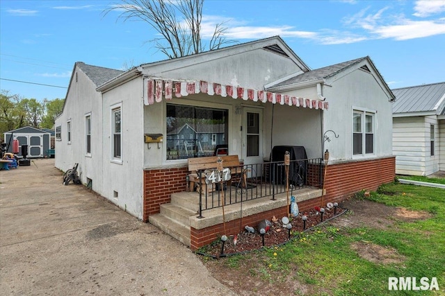 view of front facade with covered porch, an outdoor structure, a storage shed, and stucco siding