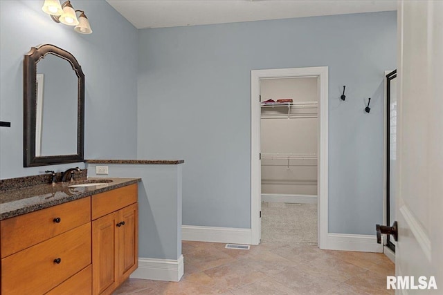 full bath with vanity, visible vents, a walk in closet, a stall shower, and baseboards