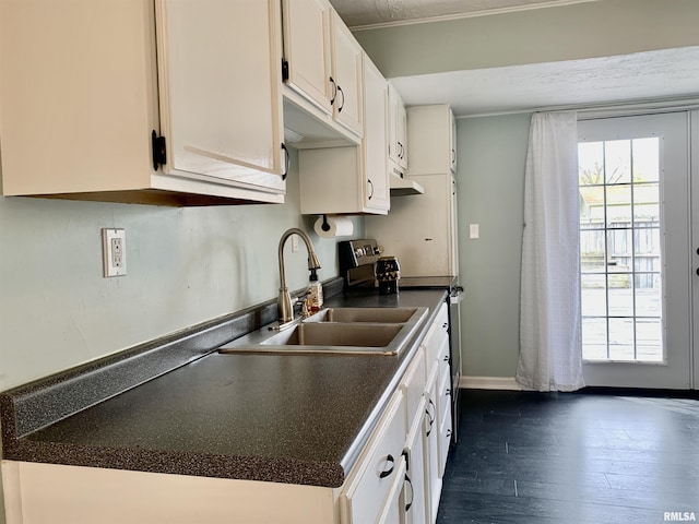 kitchen featuring dark countertops, a sink, white cabinetry, dark wood finished floors, and under cabinet range hood