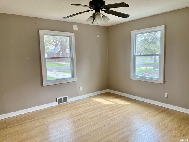 unfurnished room with wood finished floors, visible vents, a ceiling fan, and a wealth of natural light