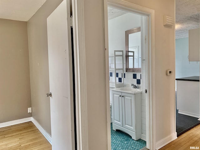 hallway featuring light wood-style flooring, baseboards, and a sink