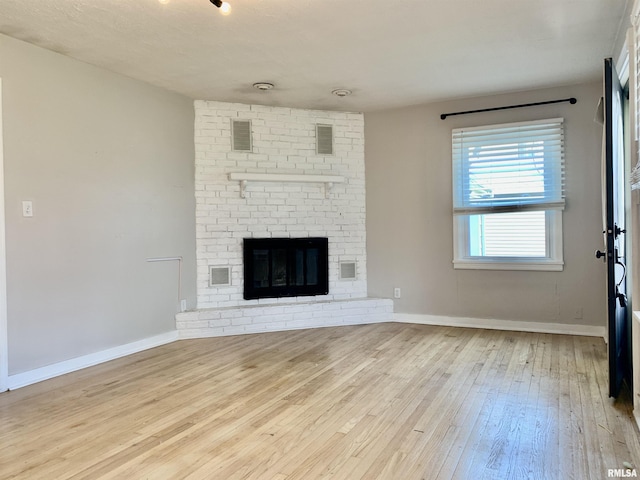 unfurnished living room with hardwood / wood-style flooring, baseboards, a brick fireplace, and visible vents