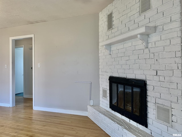 room details with wood finished floors, a brick fireplace, baseboards, and visible vents