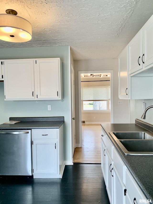 kitchen with dark wood-style floors, dark countertops, dishwasher, a sink, and white cabinetry