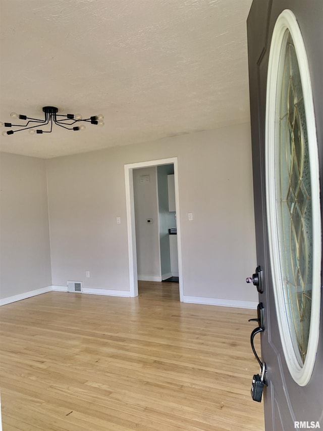unfurnished room featuring baseboards, a textured ceiling, visible vents, and light wood-type flooring