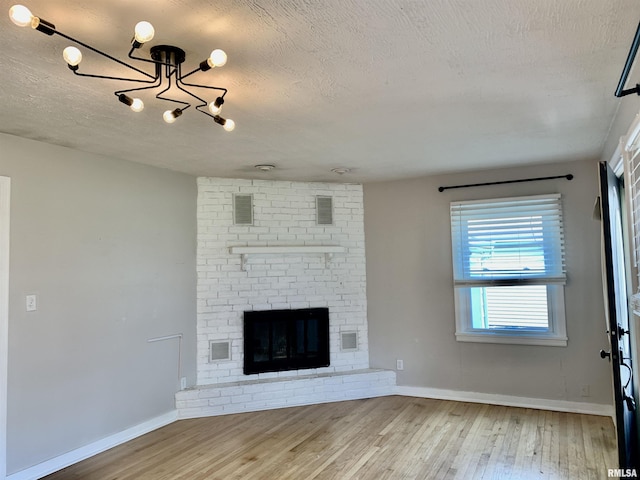unfurnished living room featuring wood finished floors, visible vents, a notable chandelier, and a brick fireplace