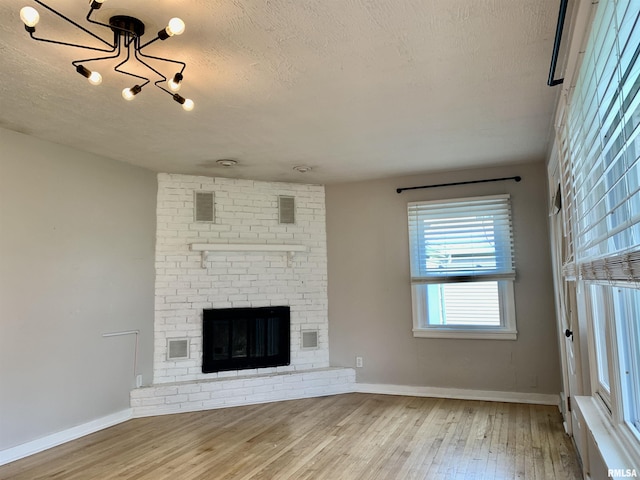 unfurnished living room featuring a textured ceiling, visible vents, baseboards, a notable chandelier, and wood finished floors