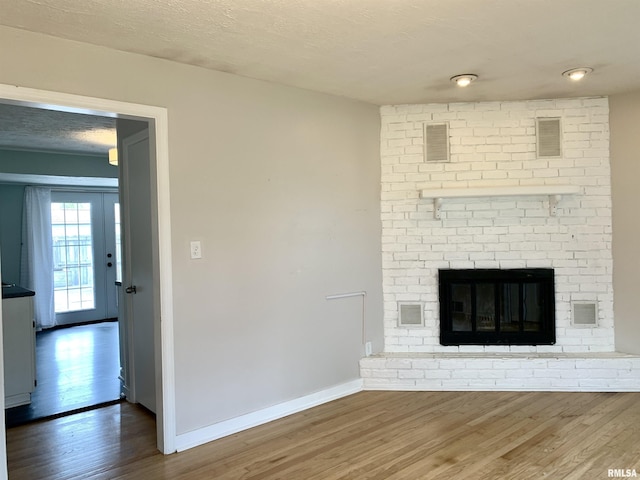 unfurnished living room with baseboards, a brick fireplace, wood finished floors, and visible vents