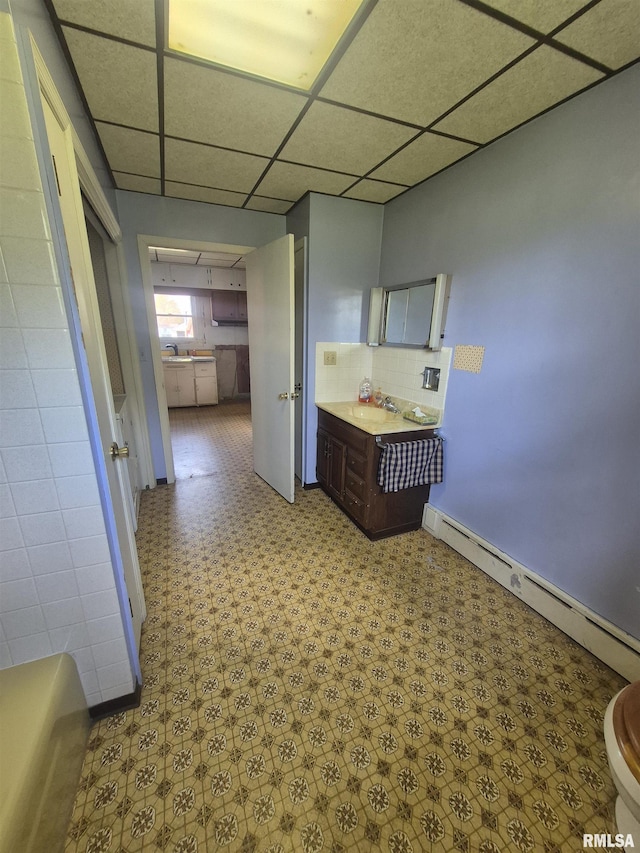 bathroom with baseboard heating, tasteful backsplash, tile patterned floors, vanity, and a drop ceiling