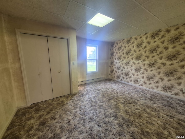 unfurnished bedroom featuring a baseboard heating unit, baseboards, carpet, and a drop ceiling