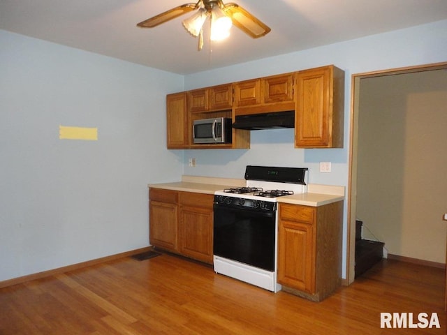 kitchen with a ceiling fan, brown cabinets, gas range oven, stainless steel microwave, and under cabinet range hood