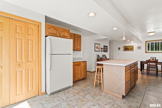 kitchen with recessed lighting, light countertops, a breakfast bar, freestanding refrigerator, and a kitchen island