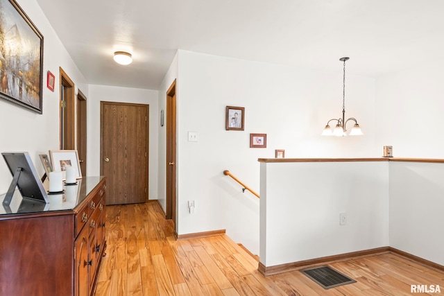 hall featuring light wood-style flooring, visible vents, an inviting chandelier, and an upstairs landing