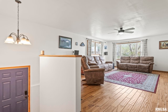 living area featuring ceiling fan with notable chandelier, light wood-style flooring, and baseboards